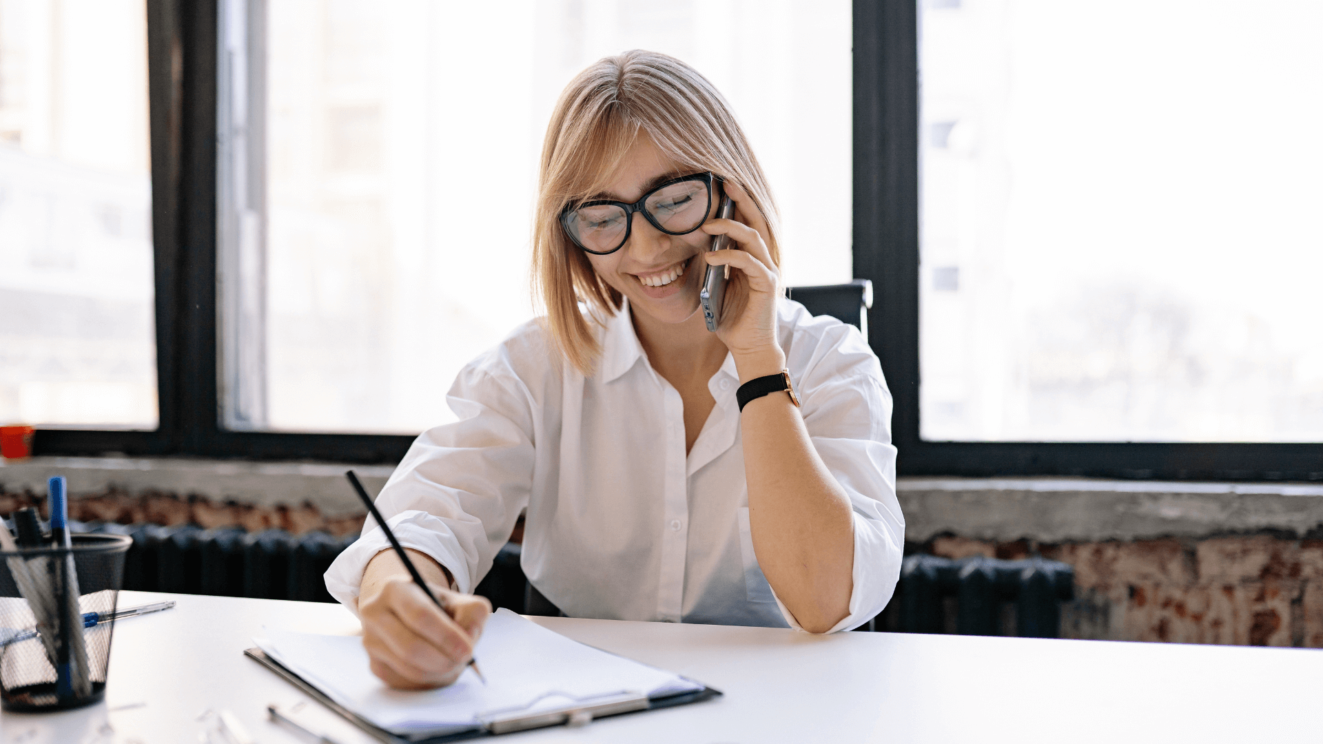 Businesswoman taking notes while speaking on the phone at her desk